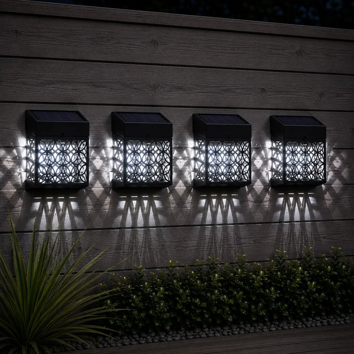Four solar-powered outdoor lights on a wooden surface with shadows.